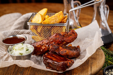 Grilled barbecue ribs with potato wedges and sauces on a wooden board