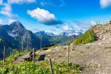 wooden park bench on mountain foot path with interesting panoramic view to the rocky mountains from Vorarlberg. the mountain Aries stone behind, interesting sky with waves clouds