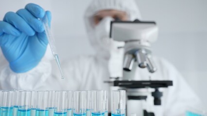 Scientific researcher wearing protective gear, carefully pipetting liquid into test tubes while conducting medical research experiment in laboratory. Medicine, healthcare and science concept