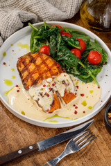 Grilled fish with creamy sauce and spinach on white plate
