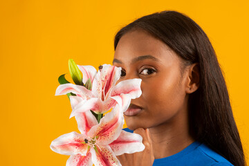 Young woman holding pink and white lily flowers on yellow background
