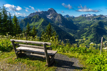 wooden park bench on mountain foot path with interesting panoramic view to the rocky mountains from Vorarlberg. the mountain Aries stone behind, interesting sky with waves clouds
