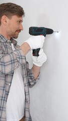 Middle aged male professional worker wearing grey checked shirt and white gloves, is drilling hole...
