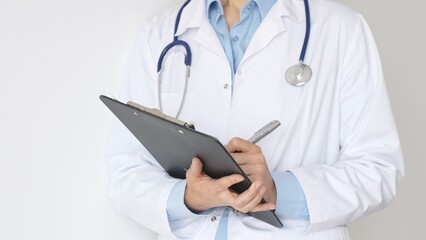 Unknown female doctor wearing stethoscope and white coat over blue blouse is standing and writing...