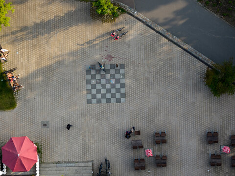 Aerial view of a checkered square contrasting sharply with the surrounding pavement, as people relax and chat in the open space, Berlin, Volkspark Friedrichshain, Germany.