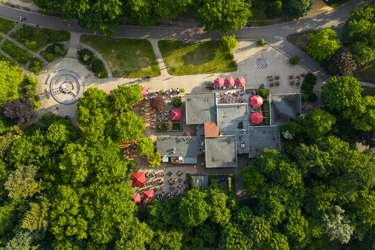 Aerial view of a vibrant cafe nestled amidst lush green trees, with red umbrellas providing a striking contrast, Friedrichshain-Kreuzberg, Berlin, Volkspark Friedrichshain, Germany.