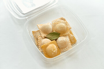 A Close-Up View of Freshly Made Ravioli with a Bay Leaf Infused in a Transparent Container Ready for Cooking or Serving
