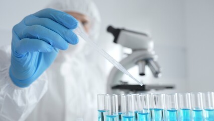 Fototapeta premium Scientific researcher wearing protective gear, carefully pipetting liquid into test tubes while conducting medical research experiment in laboratory. Medicine, healthcare and science concept
