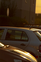 In a picturesque scene, a row of various cars is neatly parked in a spacious parking lot as the sun sets on the horizon, casting a warm glow over them