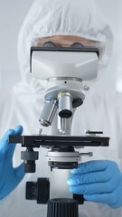 Male scientist virologist wearing hazmat suit, mask, and blue gloves, diligently working at a microscope in a laboratory researching viruses. Medicine and science concept