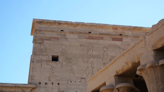 Entrance gate of the famous temple in "Philae" island, Aswan Egypt. Several symbols on the high walls. Columns on the right. Blue sky on the background.