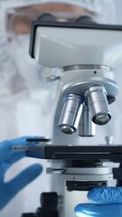 Medical virologist in a hazmat suit, mask, and gloves, diligently working at a microscope in a laboratory researching viruses. Healthcare and science concept