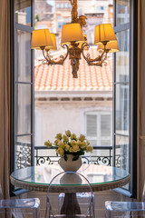 Elegant dining table with white roses by open window overlooking Mediterranean architecture — luxurious French lifestyle