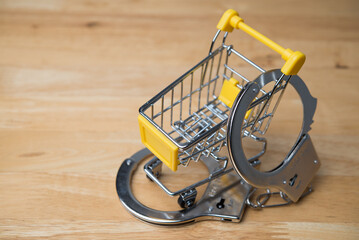 Handcuffs locked shopping cart on wooden table background copy space. Punishment for shoplifting,...