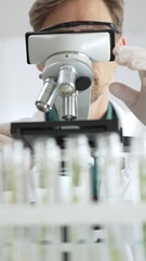Man scientific researcher in protective gear analyzing specimens through a microscope in a sterile...