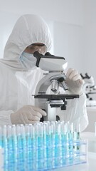 A medical virologist in protective gear examines viral samples under a microscope while conducting...