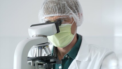 Laboratory scientist analyzing medical sample, wearing green protective gear and conducting...