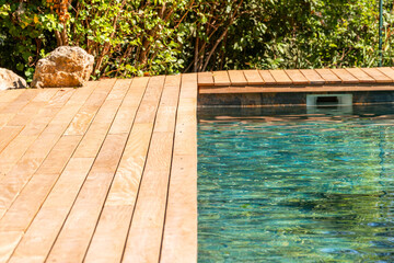 Wooden deck and natural swimming pool water in sunny garden setting