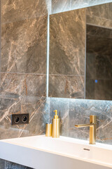 Elegant modern bathroom with marble wall tiles, illuminated mirror and gold faucet – luxury design inspiration for real estate, interior blogs, decor brands and upscale lifestyle visuals