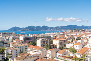 Fototapeta premium Panoramic aerial view of Cannes city and the Esterel mountains with clear blue sky and sea, French Riviera coastline, urban and nature mix, perfect for tourism, real estate, editorial or business use