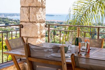 Elegant outdoor dining with sea view on the French Riviera — rustic stone column, wooden table setting, palm tree and sunshine for a perfect Mediterranean lifestyle moment