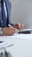 Businessman using calculator and taking notes recording financial data in office environment. Audit...