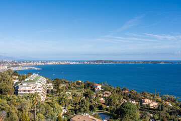 Obraz premium Scenic aerial view of luxury coastal residences and the Bay of Cannes under a bright blue sky with lush greenery and Mediterranean charm