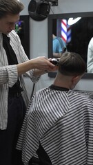 Professional barber carefully trimming customer's hair with electric clipper, providing a stylish...