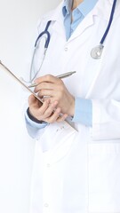 Unknown female doctor wearing stethoscope and white coat over blue blouse is standing and writing...
