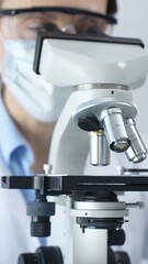 Scientist wearing lab coat and protective glasses using a modern microscope in a laboratory...
