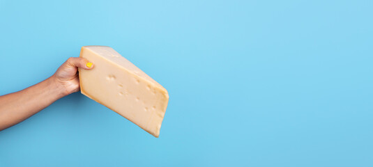  Female hand with yellow nail polish holding a large wedge of cheese against a plain light blue...