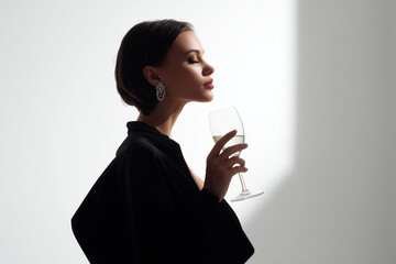 Elegant woman in black dress enjoying a glass of white wine with closed eyes in a minimalist setting