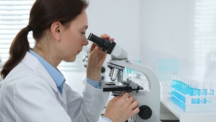 Female scientist examining microscope slide, analyzing chemical sample in sterile laboratory...