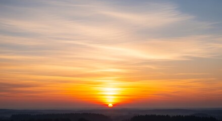 Fototapeta premium A vibrant sunset with orange and yellow hues painting the sky above a dark silhouetted landscape