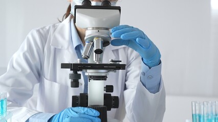 A female scientist in protective gear adjusts a microscope lens and accurately analyzes medical...