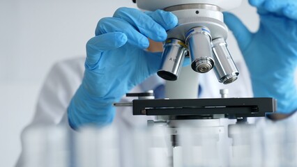 Close up of scientist's gloved hands adjusting microscope, conducting research in laboratory with...