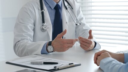 Male doctor explaining diagnosis, gesturing with hand to patient during consultation in clinical...