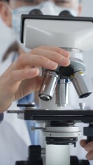 Female scientist wearing lab coat and protective glasses using a modern microscope in a laboratory...