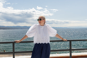 Young woman in stylish summer outfit enjoys sunny day by the sea, with sparkling water and distant...