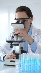 Female scientist examining microscope slide, wearing protective gear in laboratory, researching...