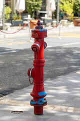Bright red fire hydrant stands prominently on sidewalk, showcasing vibrant colors and urban...