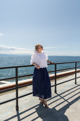Woman in stylish summer outfit enjoys sunny day by the ocean, standing on a deck with a beautiful view of the water and sky