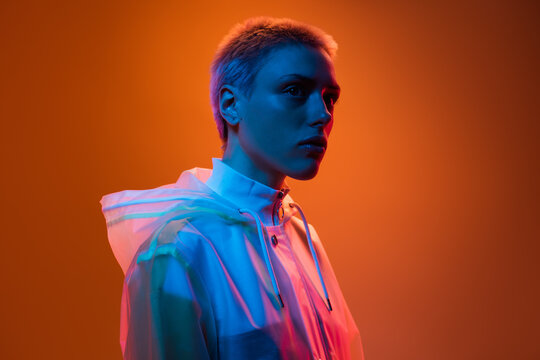 A contemporary portrait of an individual wearing a hooded garment in vivid lighting, showcasing a modern and artistic visual style with bold colors and striking contrast against an orange gradient