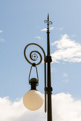Vintage street lamp with decorative design and round glass shade against a clear blue sky, showcasing urban architectural elegance and charm
