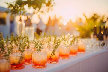 Festive beverages sit on a table, garnished with rosemary and bathed in sunset light.