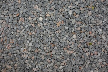 Close-up view of small gray and reddish gravel stones forming a textured ground surface. Natural rock background ideal for construction, landscaping, or decorative design concepts.