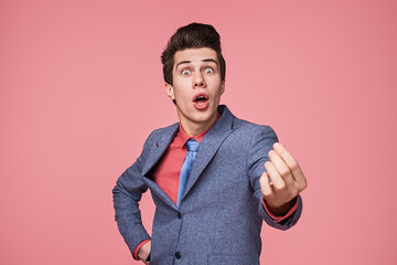 A man in a blue suit and colorful tie gestures expressively, posing against a bold pink backdrop....