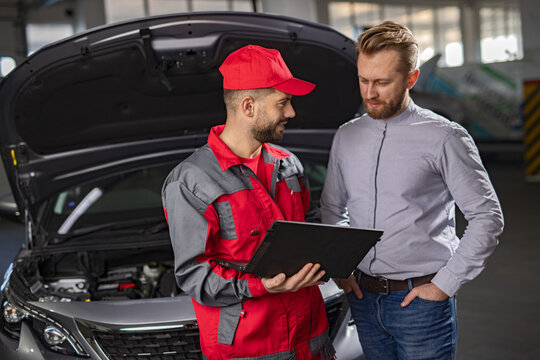 A mechanic in uniform shows a customer vehicle repair details on a tablet in the workshop.