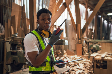 African American Man Working in Timber Factory Performing Quality Inspection on Wooden Planks with...
