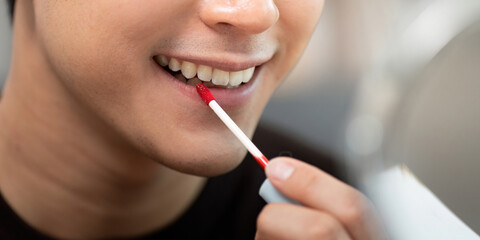 Grooming. Young man applying red lip gloss with precision.